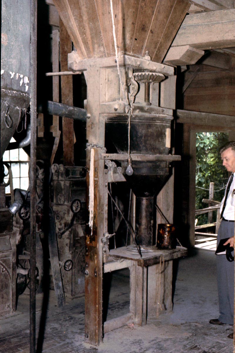 Carl Stoneburner stands next to the flour packer. The two roller stands are visible to the left